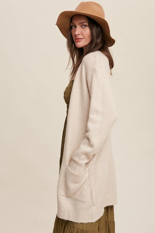 Cozy, natural solid-colored long knit cardigan with an open front, two functional pockets, and long sleeves.