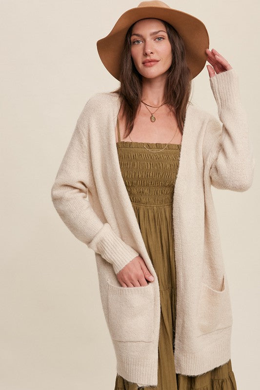 Cozy, natural solid-colored long knit cardigan with an open front, two functional pockets, and long sleeves.