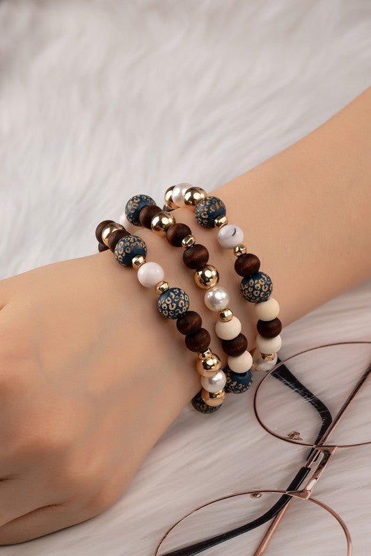 Woman wearing Livia Wood Carved Animal Print Bracelet Set with blue leopard wood beads, acrylic pearls, and CCB beads.