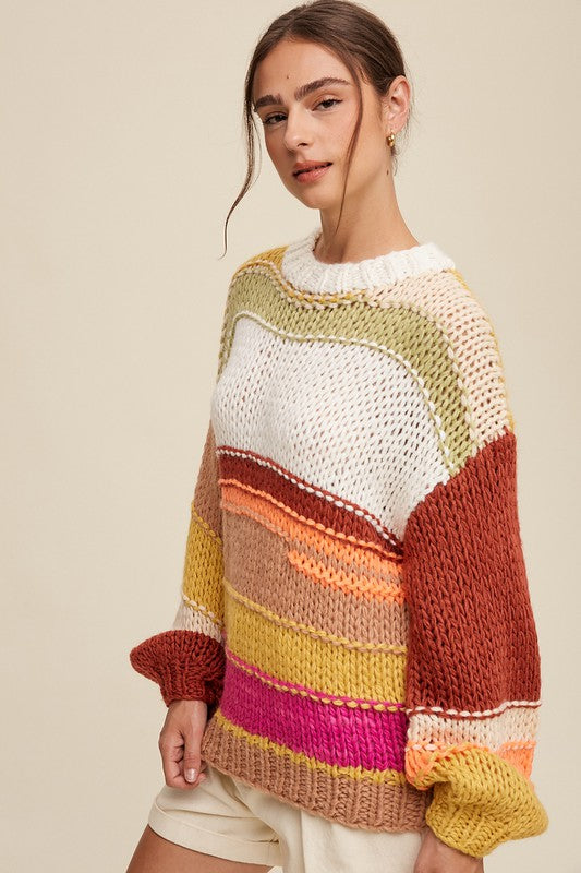 A cozy crochet sweater with a relaxed fit, featuring a round neckline accented with ribbed detailing. The long sleeves and hip-length silhouette create a comfortable and stylish look. The pullover design showcases vibrant stripes in shades of green, red, white, orange, and yellow, adding a playful and colorful touch.