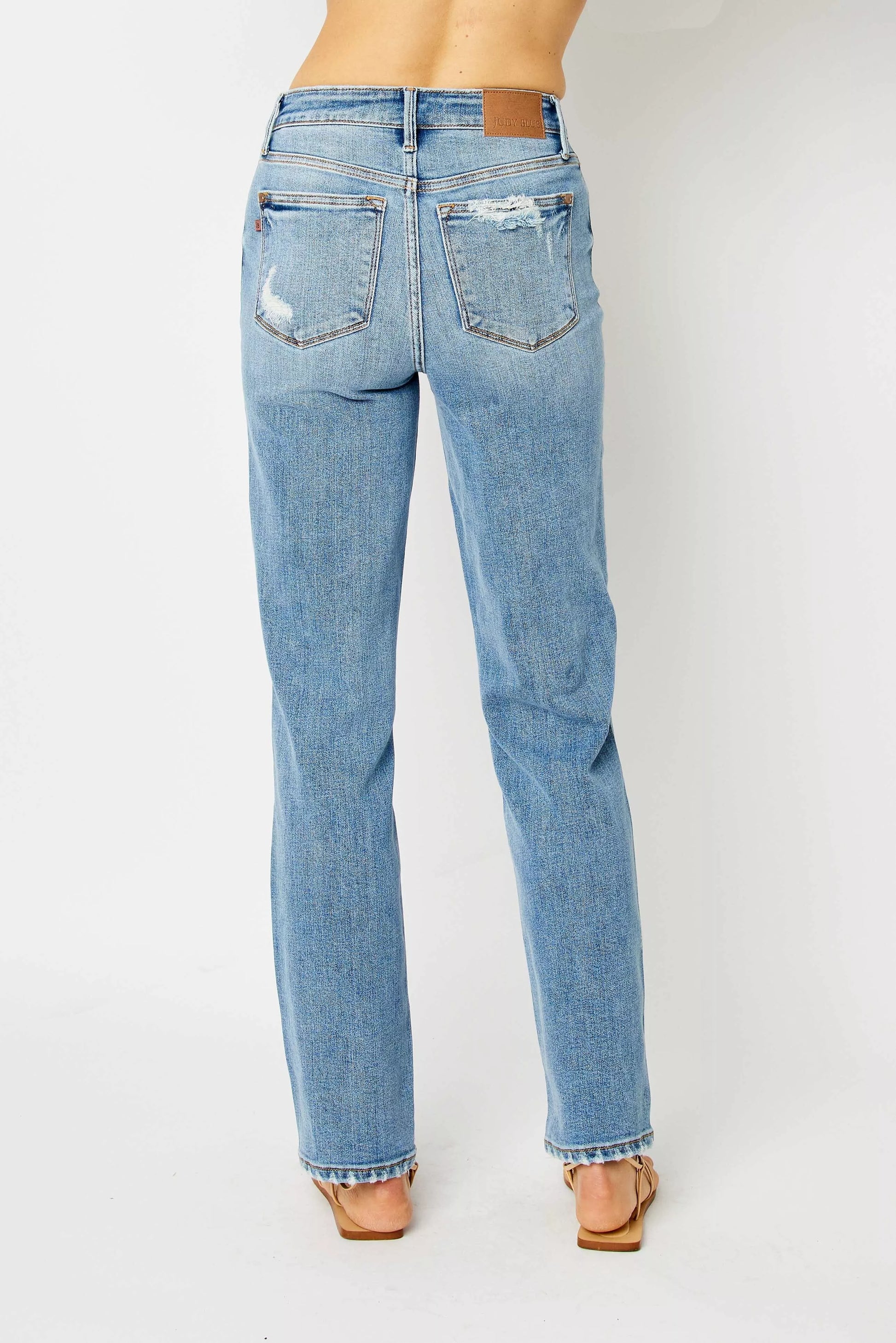 Back view size inclusive Estee Judy Blue jeans, medium wash straight cut with raw hem detail.