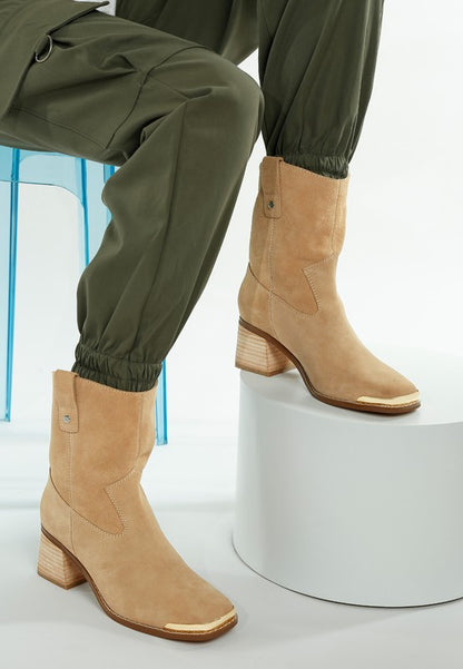 Model lifting leg to show comfort fit and pull-tab design on beige Emberly boots.