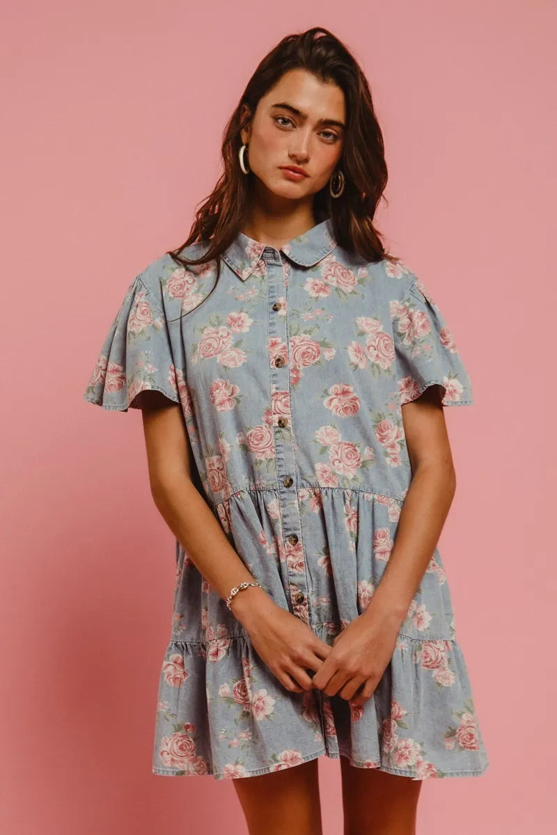 Close-up of Isla Floral Tiered Shirt Dress by BiBi, featuring button-front closure, collared neckline, and delicate pink floral print on denim blue.