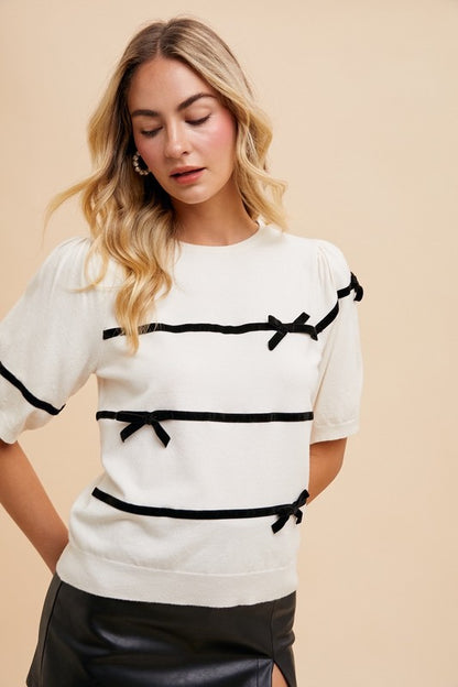 Bernadette Striped Bow Knit Top in white with black stripes, featuring feminine bow details, round neckline, short sleeves, and ribbed knit for a chic, comfortable style.