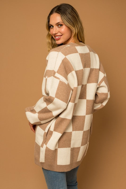 A long open-front cardigan made of knit fabric with a taupe and white checker pattern. It features long sleeves, side pockets, and a relaxed, medium long length