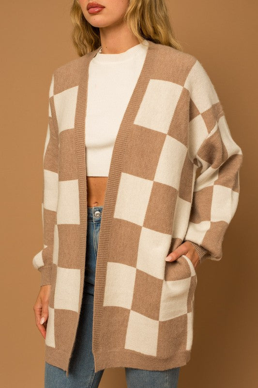 A long open-front cardigan made of knit fabric with a taupe and white checker pattern. It features long sleeves, side pockets, and a relaxed, medium long length