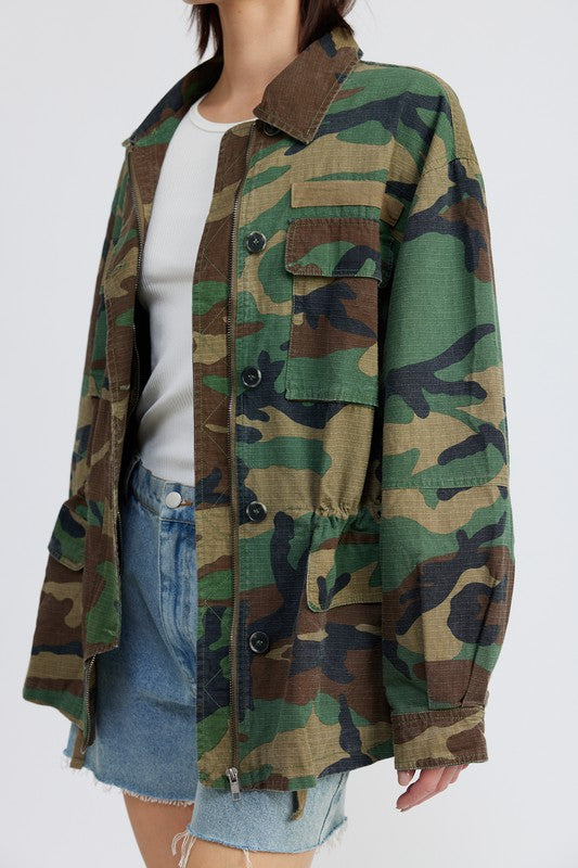 Oversized camo jacket with a collared neckline, long sleeves, and practical pockets. Made of 100% cotton with zipper and button closures.