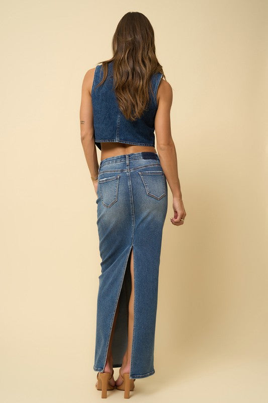 Dark wash denim maxi skirt with a five-pocket design and a back slit for added movement. Features a mid-rise waist, button and zipper fly closure, and a regular fit.