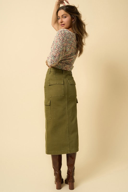 Olive green denim cargo midi skirt with a front slit and seven functional pockets. Features a button closure and regular fit.