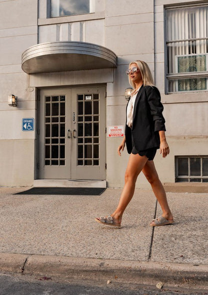 A stylish motion shot capturing a pretty woman walking in the Kelly Houndstooth Slides in nude, showcasing their casual elegance and comfortable fit in an everyday outfit.