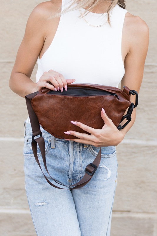 Chsetunt sling bag with a soft vegan leather exterior, chunky black chain accent, and adjustable strap. Includes zip pockets and a solid design.