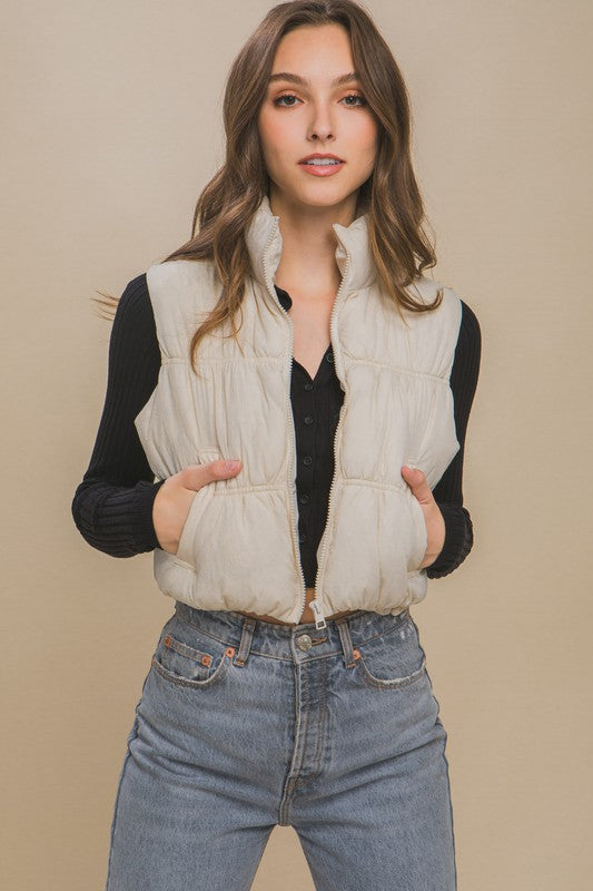 Cream sleeveless puffer vest with a high collar, cropped length, and side pockets.