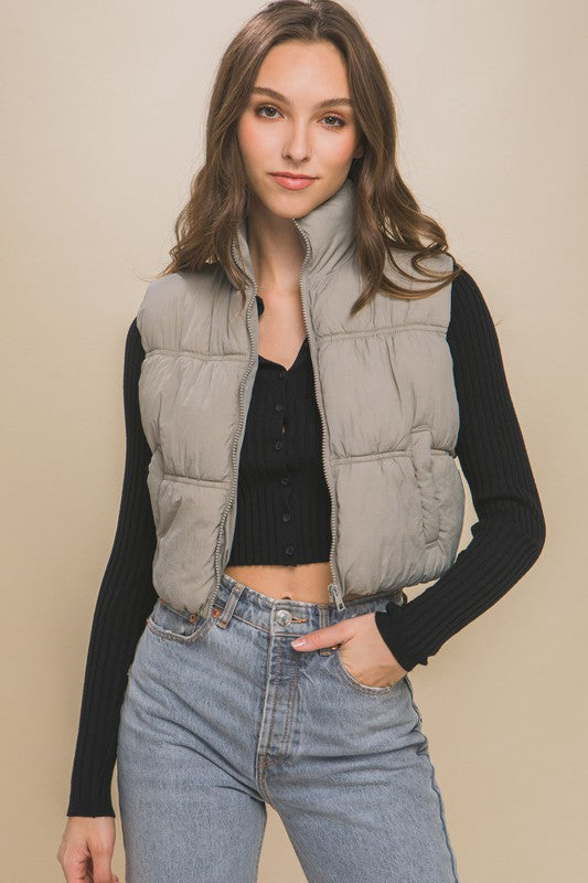 Grey sleeveless puffer vest with a high collar, cropped length, and side pockets.