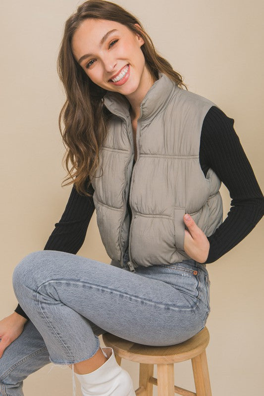 Grey sleeveless puffer vest with a high collar, cropped length, and side pockets.