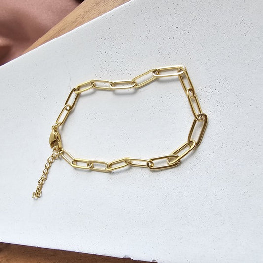 Gold paper clip bracelet displayed on a white background, showcasing its modern linked design.