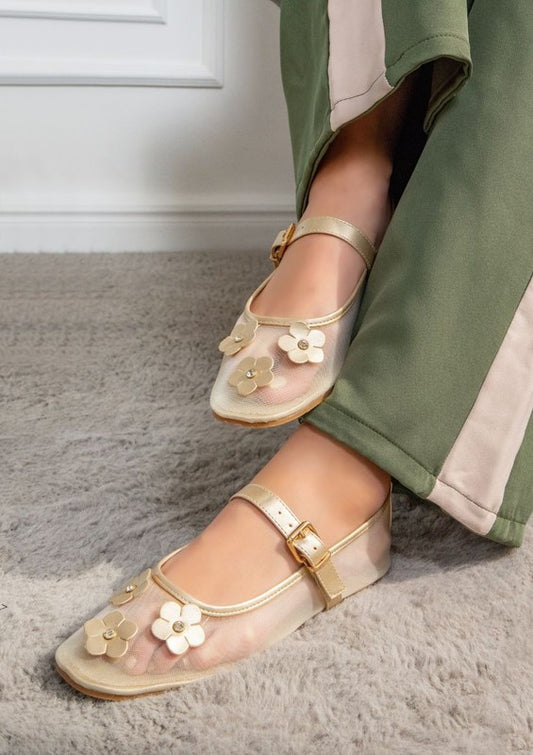Woman wearing gold mesh Mary Jane flats with floral detail and secure strap.