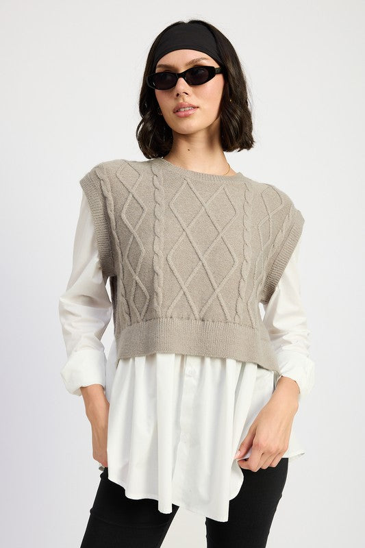 Gray cropped cable knit vest layered over a long white faux button-up shirt with a round neckline and long sleeves.