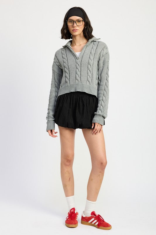 Cropped cable knit sweater in grey with a half-zip neckline, drop-shoulder long sleeves, and a ribbed hem.