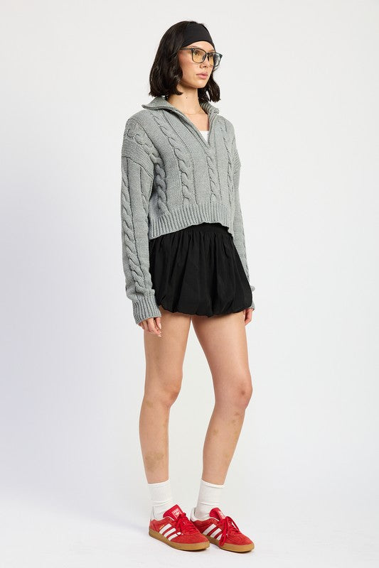 Cropped cable knit sweater in grey with a half-zip neckline, drop-shoulder long sleeves, and a ribbed hem.