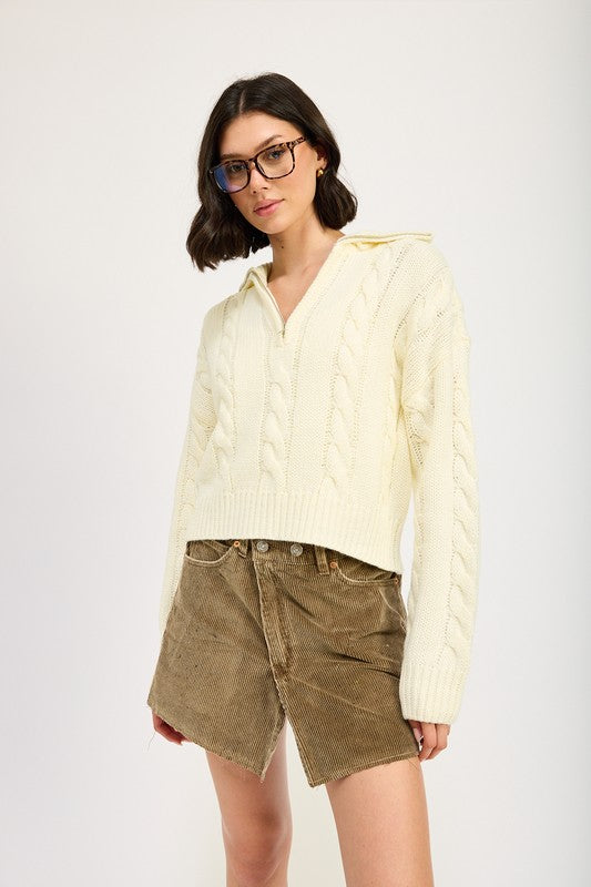 Cropped cable knit sweater in cream with a half-zip neckline, drop-shoulder long sleeves, and a ribbed hem.