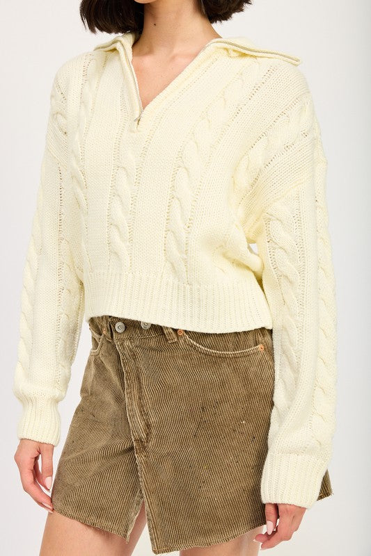 Cropped cable knit sweater in cream with a half-zip neckline, drop-shoulder long sleeves, and a ribbed hem.