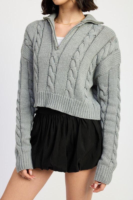 Cropped cable knit sweater in grey with a half-zip neckline, drop-shoulder long sleeves, and a ribbed hem.