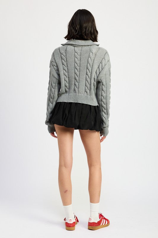 Cropped cable knit sweater in grey with a half-zip neckline, drop-shoulder long sleeves, and a ribbed hem.