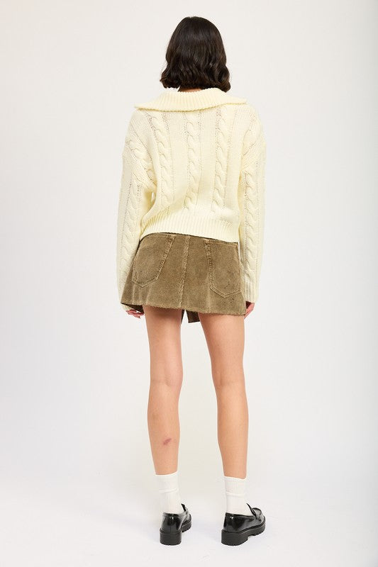 Cropped cable knit sweater in cream with a half-zip neckline, drop-shoulder long sleeves, and a ribbed hem.