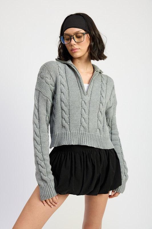 Cropped cable knit sweater in grey with a half-zip neckline, drop-shoulder long sleeves, and a ribbed hem.