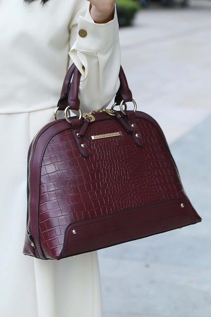 Model holding Eggplant Nora Satchel showing croco pattern and gold hardware.