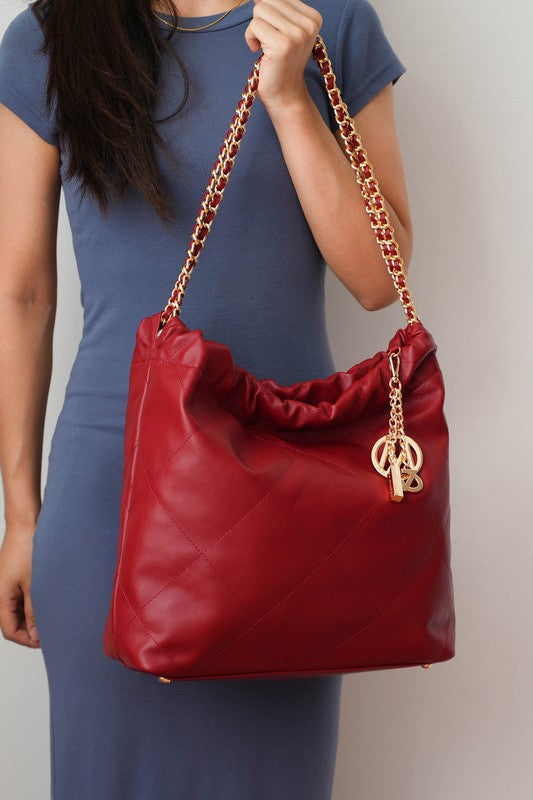 Woman holding wine MKF Celestine quilted shoulder bag by gold chain strap.