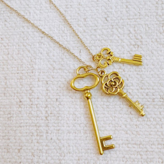 Flat lay of Secret Garden Key Necklace with three gold key pendants on delicate chain