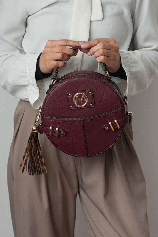 Woman holding wine MKF Gayle Crossbody Bag by top handle, showing structured shape.