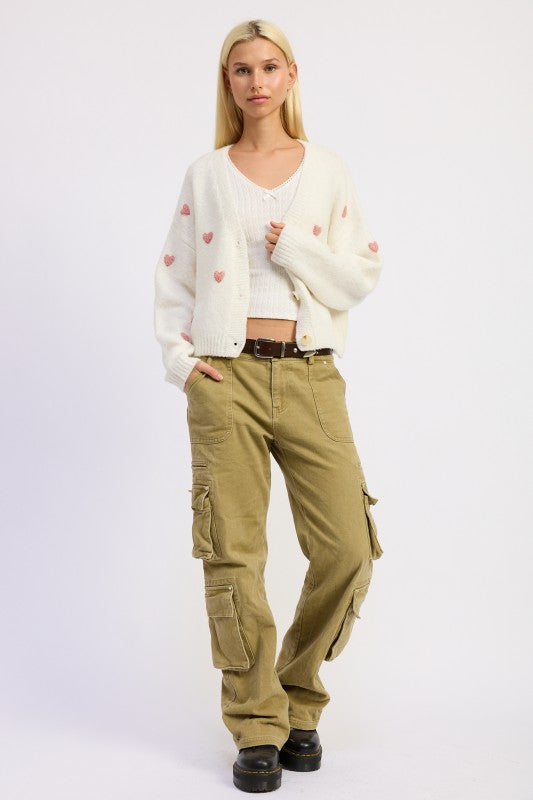 Model wearing Donna Cropped Cardigan in ivory with pink heart embroidery and button-down front.