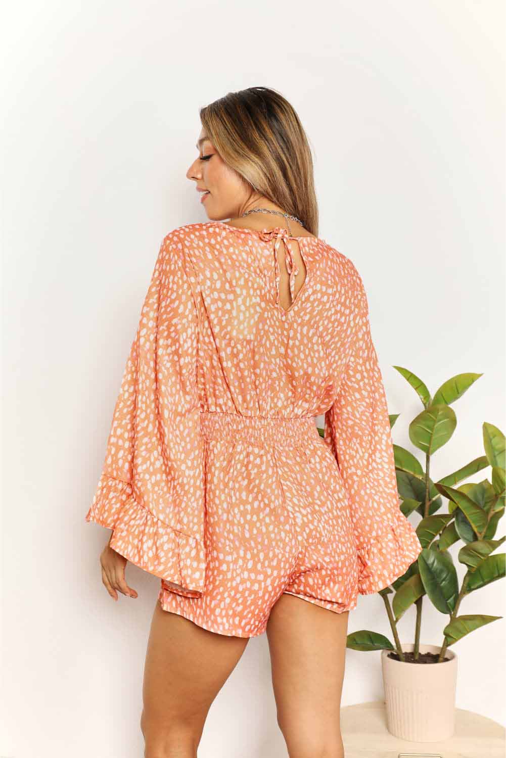 Tangerine printed romper with a surplice neckline, long flare sleeves, and smocked detailing.