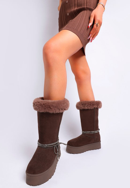 Side view of model wearing brown snow boots showing faux fur trim and tie detail.