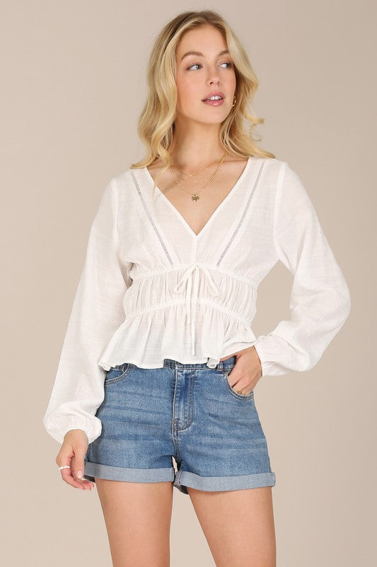 Lace top in ivory features a V-neckline, long, flowy sleeves, waist gathers, and soft ruffles at the hem.