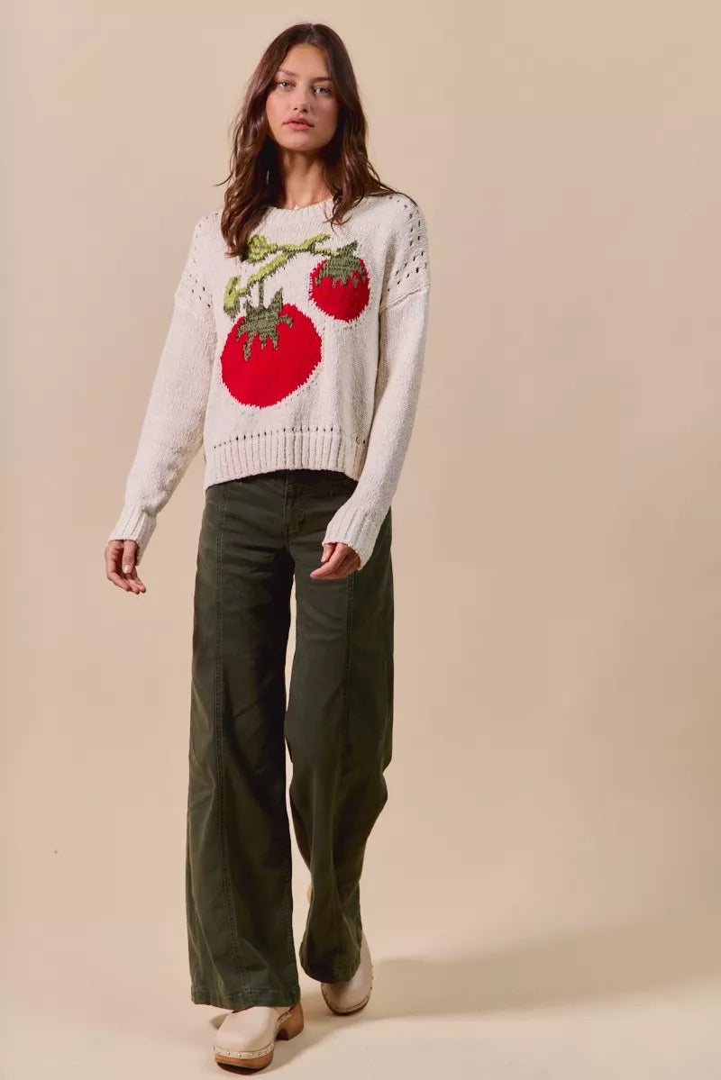 Full body view of Tara Tomato Sweater styled with dark pants, playful tomato design on cream knit