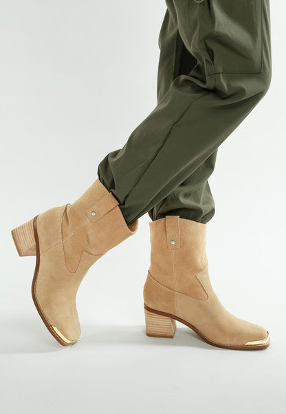 Model wearing beige Emberly suede ankle boots with gold toe cap and flared heel.