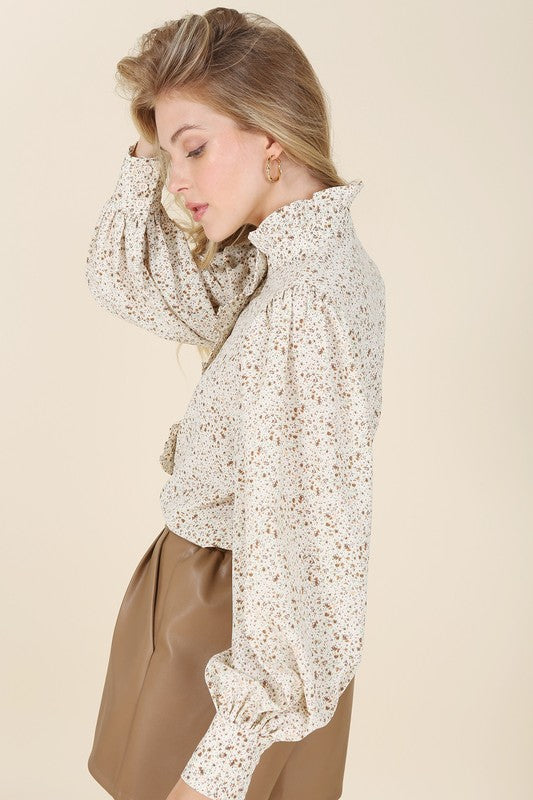 Stand Collar Floral Frill Blouse with puff long sleeves, floral pattern, and ruffled front detailing. Features shirring at the collar, shoulders, and cuffs. Button down closure.