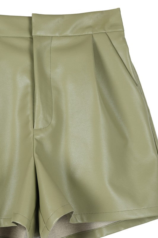 Trendy green vegan leather shorts featuring a hook and zipper closure, side pockets, pin-tuck detailing, and a comfortable wide elastic waistband.