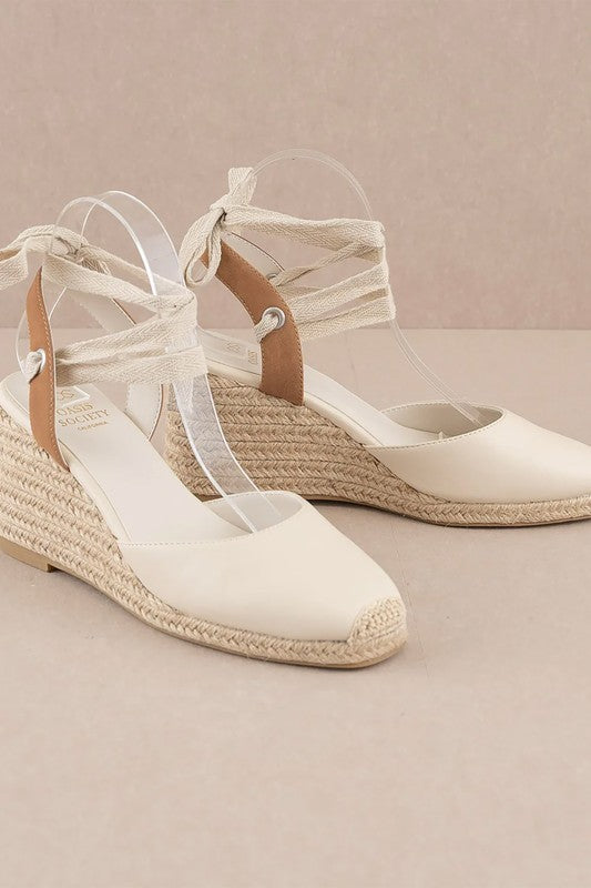 Beige espadrille wedge sandals featuring a lace-up design.