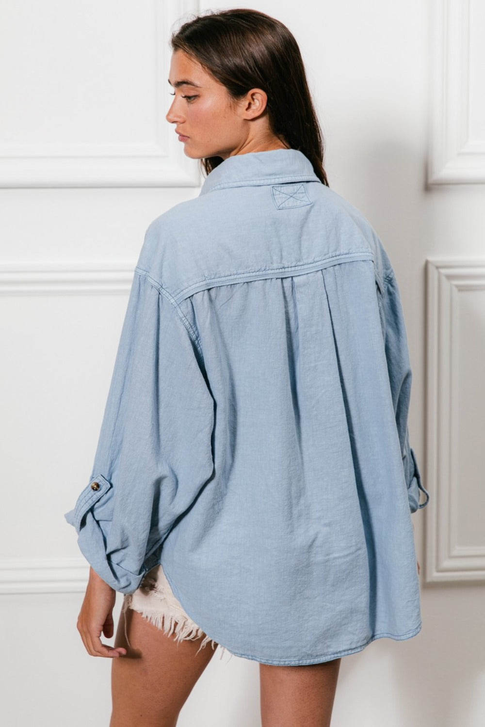 A denim button-down shirt with long sleeves, chest pockets, and detailed stitching. The shirt has a collared neckline and button closure.