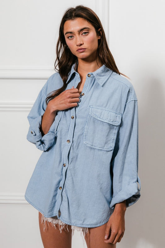 A denim button-down shirt with long sleeves, chest pockets, and detailed stitching. The shirt has a collared neckline and button closure.