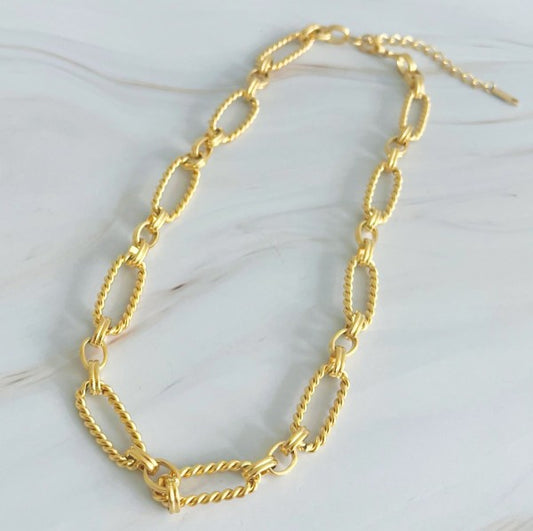 Gold alternatively linked cabled necklace laid out on marble background