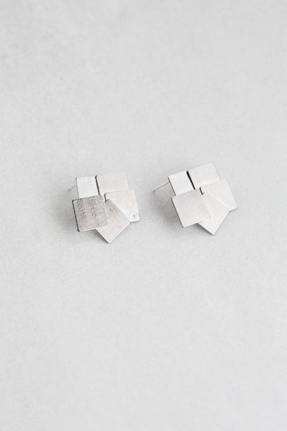 Top view of overlapping gunmetal square stud earrings.