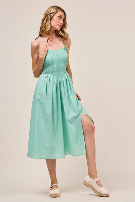Front view of the Berkley Smocked Midi Dress in sage, worn with summer espadrilles, highlighting the side slit and flowy skirt design.