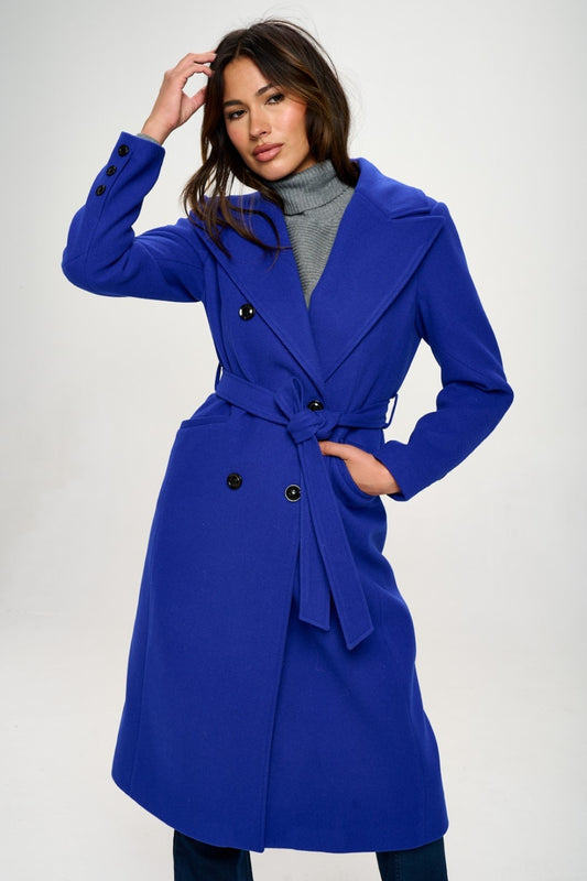 A royal blue double-breasted longline coat with a waist-cinching belt and long sleeves. The coat features a collared neckline, pocket details, and a tied closure.