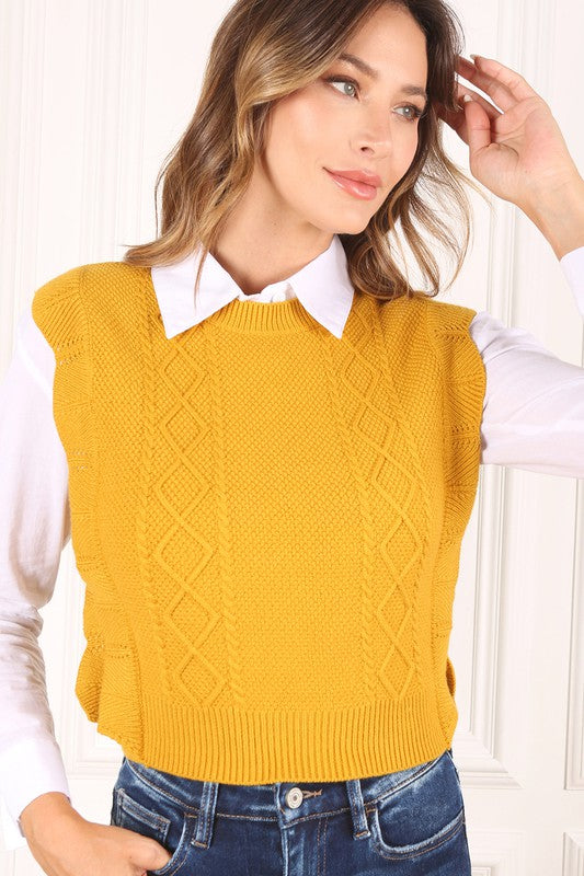 Mustard yellow sweater vest with argyle jacquard pattern, and ruffle trim on the armholes. Sleeveless with a round neckline.