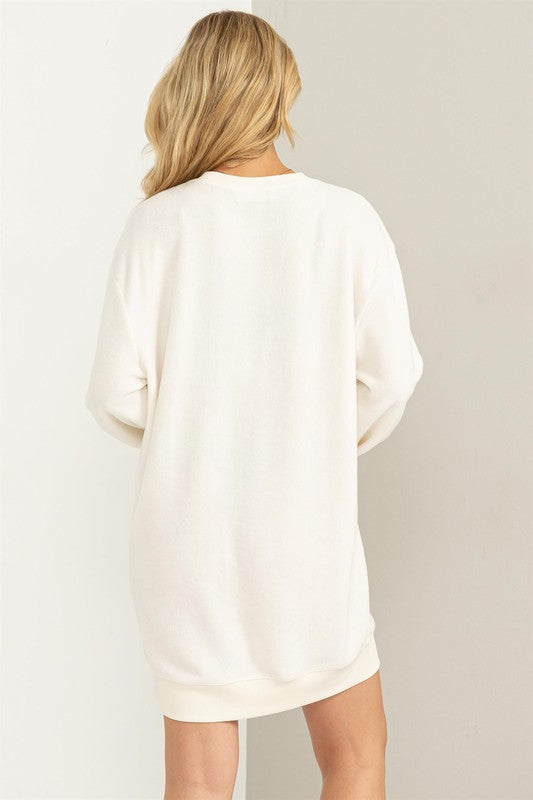 Cream-colored girlfriend sweatshirt mini dress with a crew neckline and cuffed hem, drop shoulders, long sleeves, and a relaxed fit. 